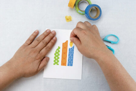 person placing cut yellow tape in a teardrop shape to make candle flame shapes on…